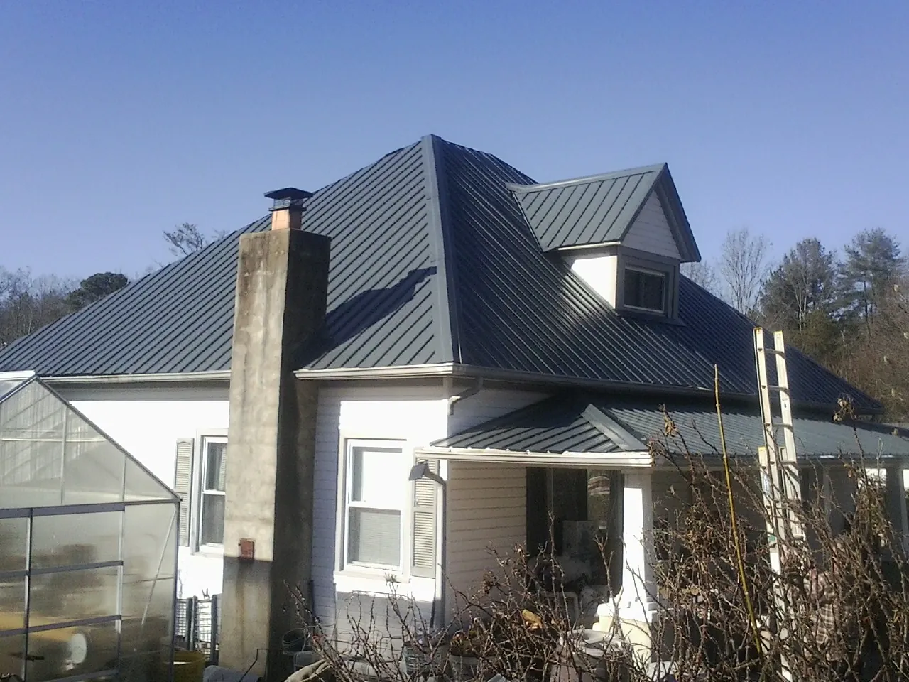 Dark blue standing seam metal roof on a white farmhouse with dormer — Slate & Tile Roof Repair by Roofing Brothers in Colts Neck