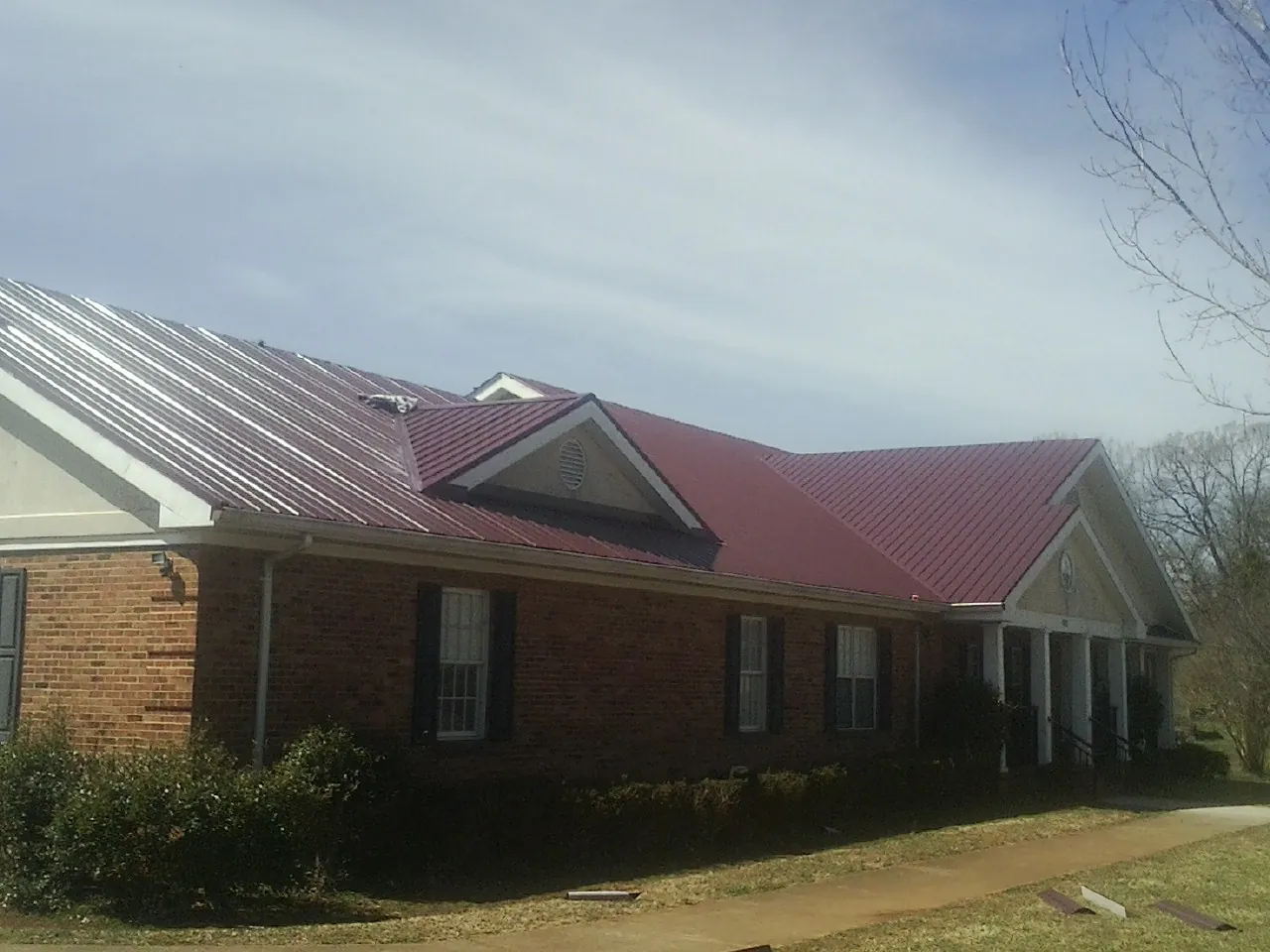 Red metal roof with gabled entries on a long brick building, from a Hail Damage Roof Repair job in Colts Neck