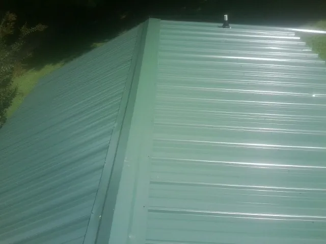 New green metal panels meeting at the ridge of a roof — Flat Roof Repair work by our crew in Colts Neck