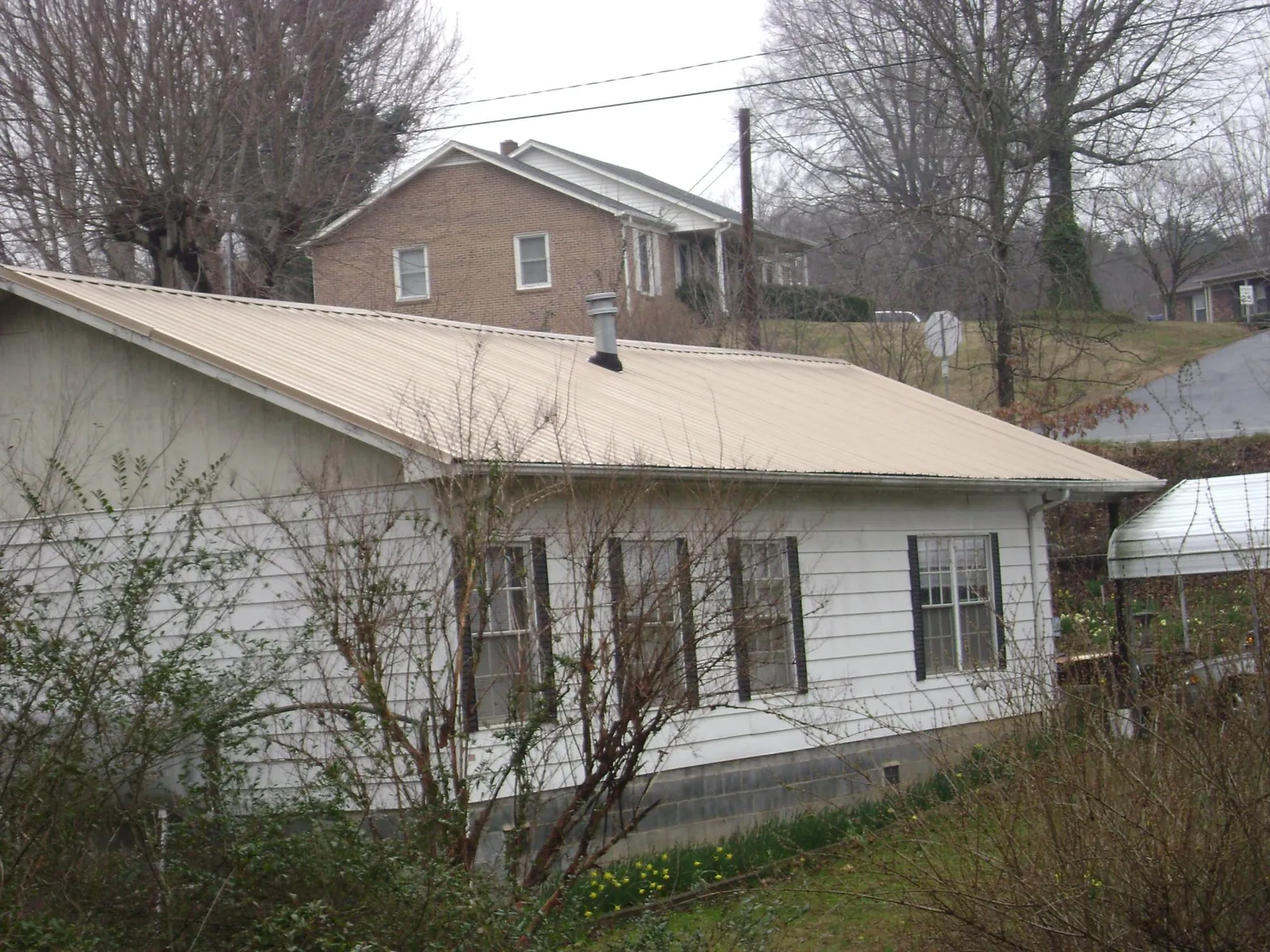 Tan metal roof on a white sided house set into a hillside — Commercial Roofing by Roofing Brothers in Colts Neck