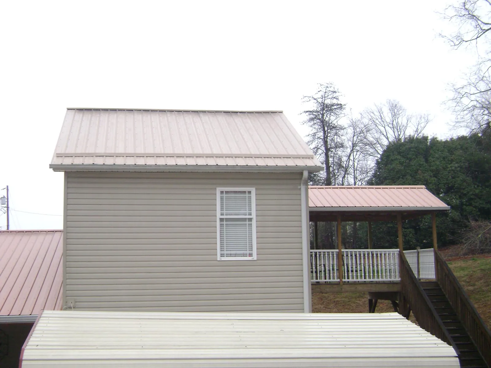 Tan metal roofs on a two story addition and attached porch, from a Roof Replacement job in Colts Neck